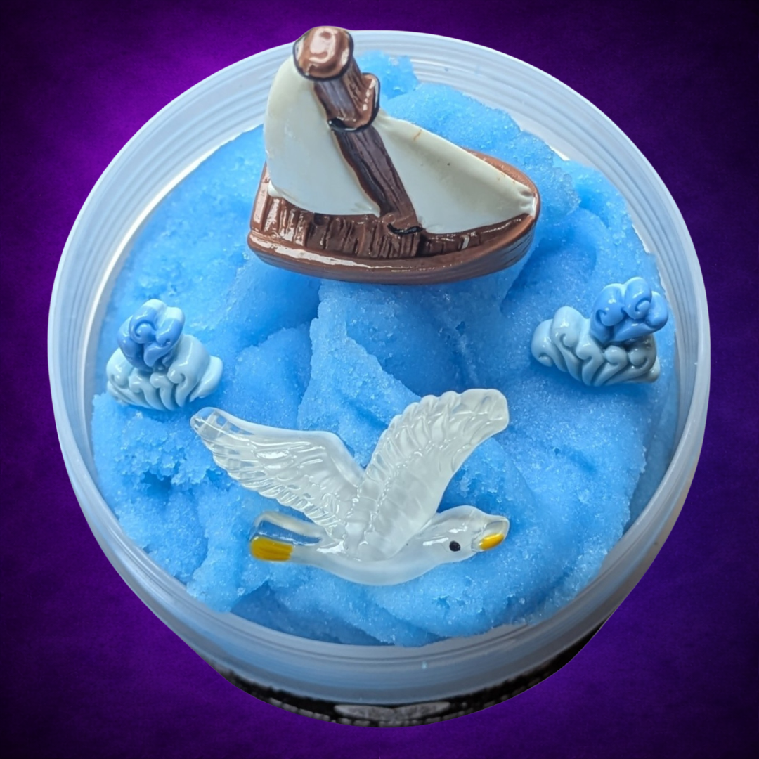 Overhead view of Beyond Nine Waves blue Icee slime with a sailboat, seagull and wave charms.